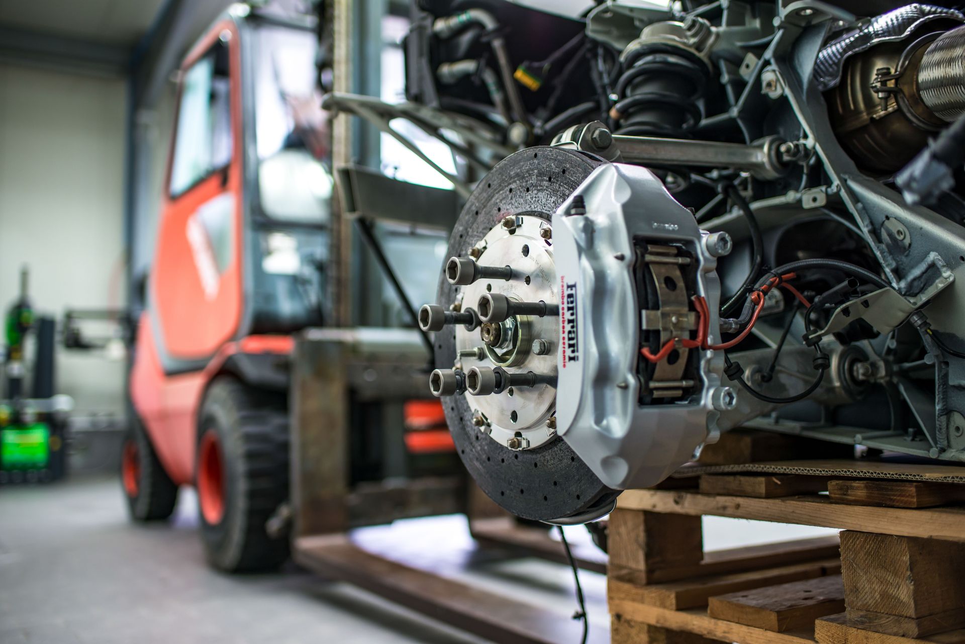 Detailed view of an automotive brake caliper and disc in an industrial workshop setting.